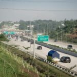 a highway filled with lots of traffic next to a lush green hillside